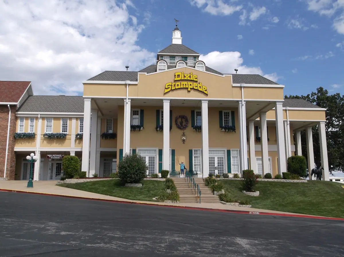 White colonnaded building with a cupola and flower beds under a blue sky in Branson