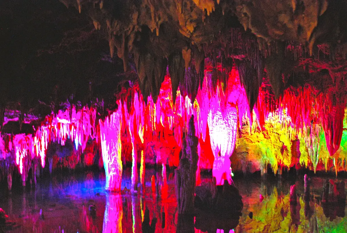 Pink and yellow floodlit stalactites reflected in the still water of Meramec Caverns