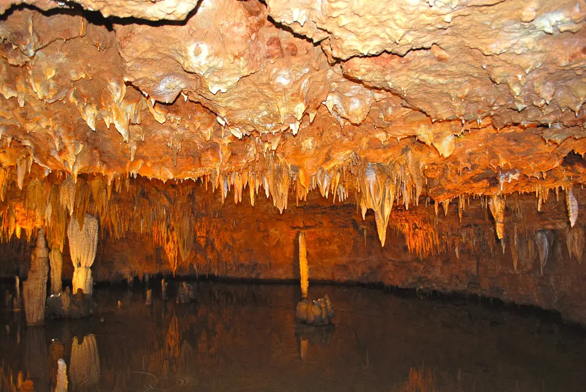 Orange cave ceiling with small stalactites above a quiet pool in Meramec Caverns